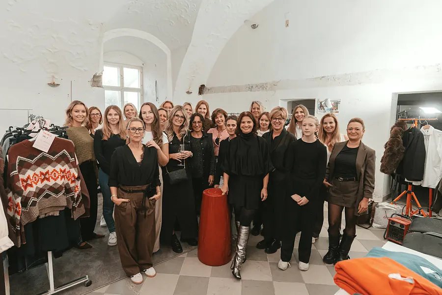 Großes Gruppenfoto im weißen Gewölberaum zwischen Kleiderstangen
