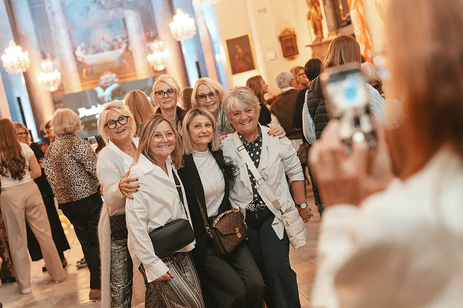 Mehrere Gäste posieren unter Kronleuchtern für ein Handyfoto