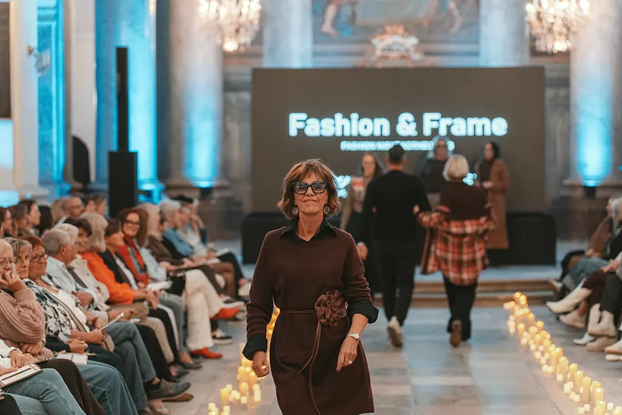 Model im braunen Kleid mit Stoffblume am Gürtel, dahinter weitere Models